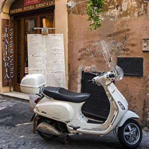 Italian Vespa scooter parked outside a trattoria restaurant in a cobblestone street